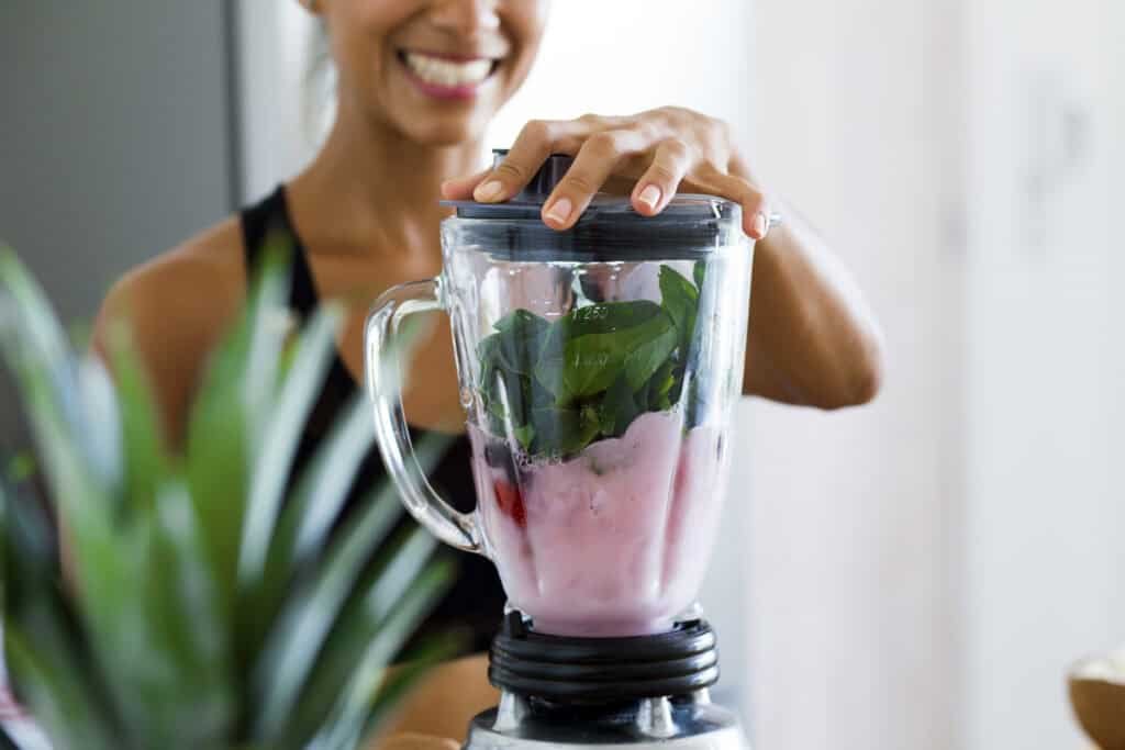 Woman prepares green smoothie with spinach and berries in blender