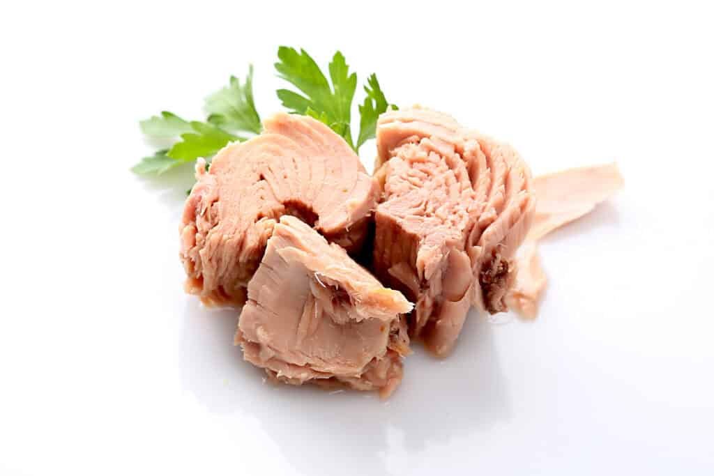 Blocks of canned tuna with fresh parsley garnish on a white background