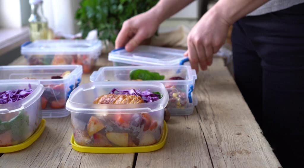 Person organizing healthy meal prep containers with grilled chicken, vegetables and colorful ingredients