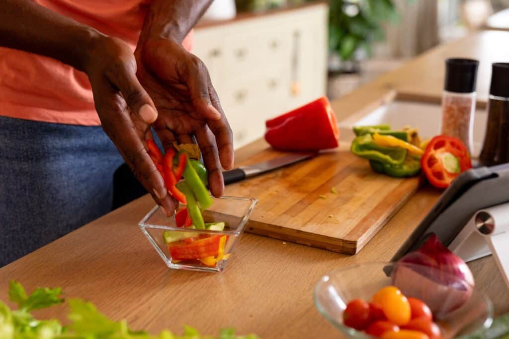 Person cuts colorful peppers on wooden cutting board in bright kitchen