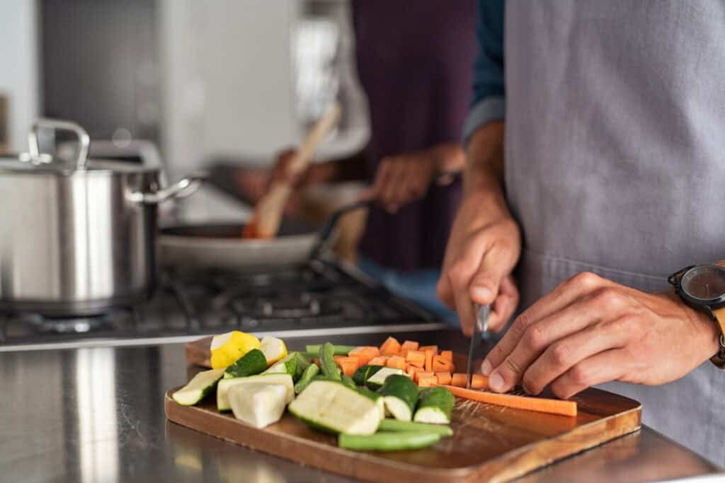 Person in apron cutting fresh carrots on wooden cutting board in modern kitchen
