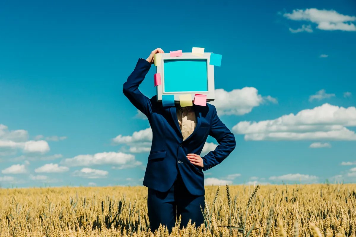 Businesswoman with retro monitor head standing in wheat field under blue sky
